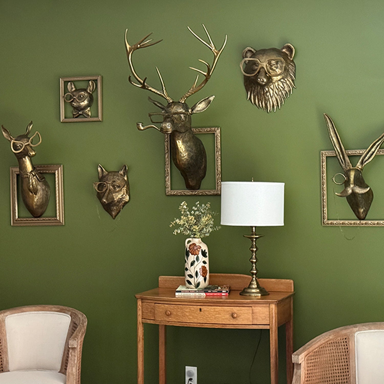 Decorative wall art with animal heads on a green wall, including a lamp and small table.